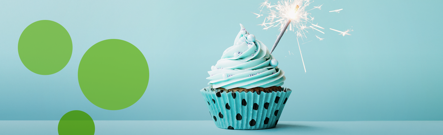 Cupcake mit brennender Wunderkerze vor türkisfarbenem Hintergrund.