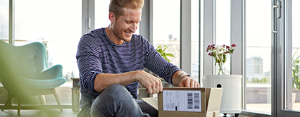 In Wohnung sitzender Mann freut sich über Paket, das er öffnet.